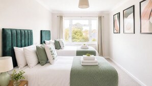 Une chambre avec deux lits, une fenêtre, une table de chevet avec une lampe et des tableaux encadrés accrochés au mur.
