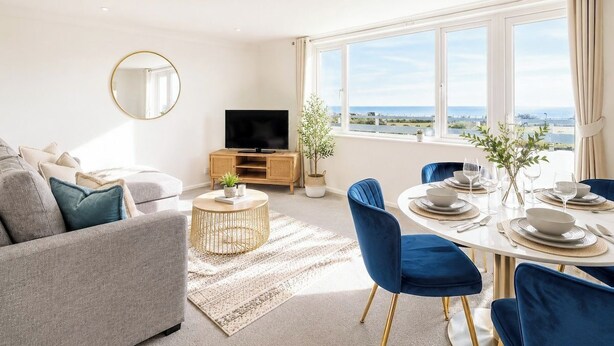 Un salon moderne comprenant un canapé, un téléviseur, une table à manger et des chaises, avec vue sur la mer.
