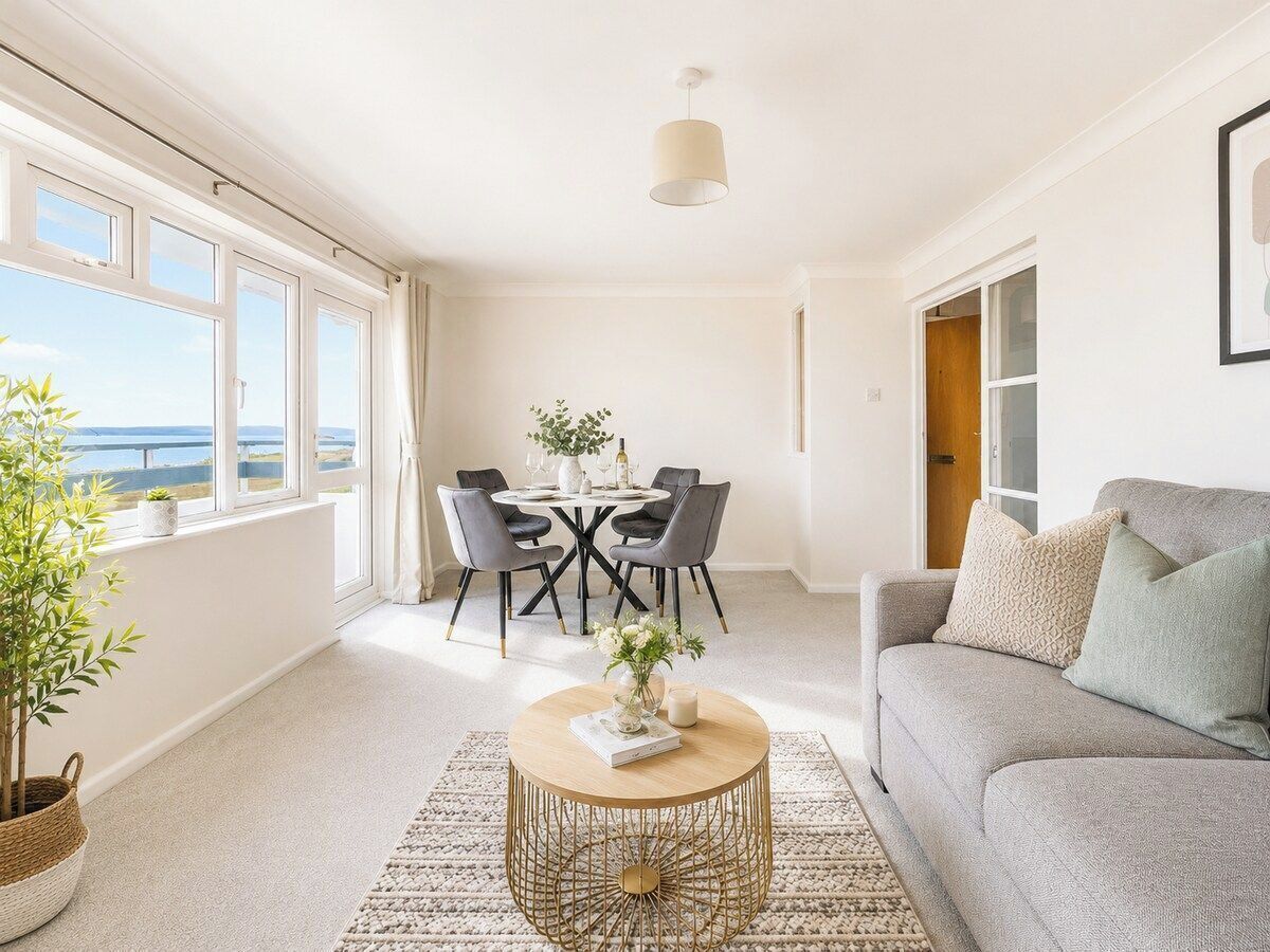 Un salon moderne avec un canapé, une table basse ronde et une table à manger avec des chaises. Une grande fenêtre offre une vue sur l’extérieur.