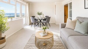 Un salon moderne avec un canapé, une table basse ronde et une table à manger avec des chaises. Une grande fenêtre offre une vue sur l’extérieur.