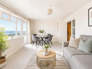 Een moderne woonkamer met een bank, een rond bijzettafeltje en een eettafel met stoelen. Een groot raam biedt uitzicht op de omgeving.