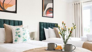 Et hotelværelse med to senge, et stort abstrakt maleri, en vase med blomster og et fad med snacks.