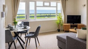 Et værelse med et spisebord dækket til fire personer, en sofa, et fjernsyn og havudsigt.