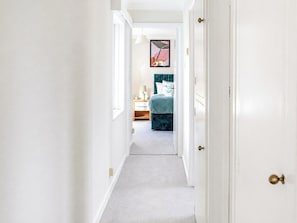 Ein schmaler Flur mit Teppichboden, der zum Schlafzimmer mit Bett und Nachttisch führt.