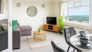 Ett modernt vardagsrum med en soffa, TV, matbord och utsikt över havet.