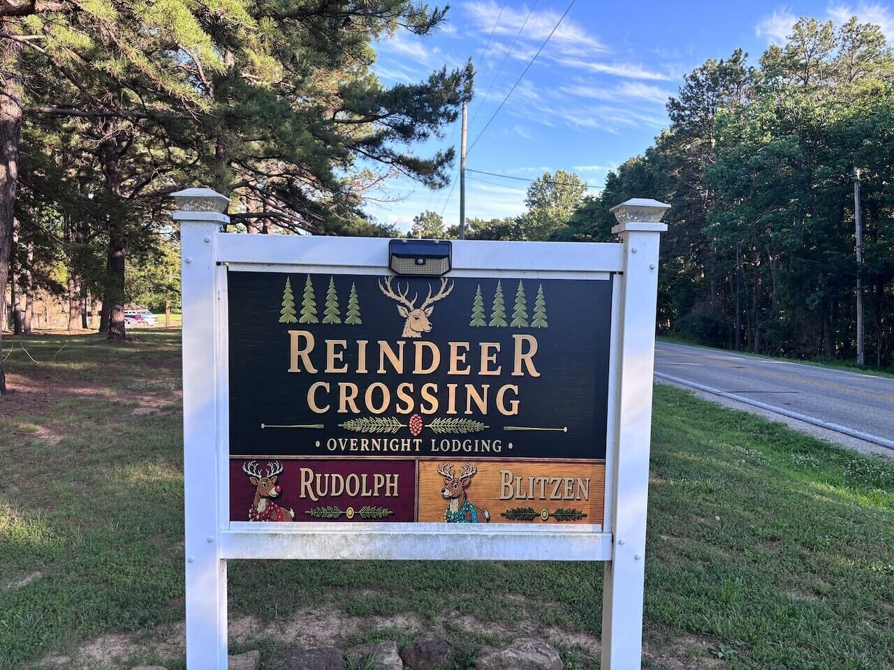 Placa para Reindeer Crossing Overnight Lodging, com um logotipo de veado, marca Rudolph e Blitzen e um cenário de floresta.