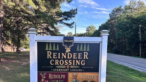 En skylt för Reindeer Crossing, ett boende där man kan övernatta, med en hjortlogotyp, varumärket Rudolph och Blitzen, och en skog i bakgrunden.