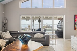 Un salon moderne avec un canapé en cuir, une table basse en bois et une vue sur l’océan grâce à de grandes fenêtres.