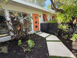 Ein modernes Haus mit einer auffälligen orangenen Tür, einem schwarzen Zaun und einem Garten mit verschiedenen Pflanzen.