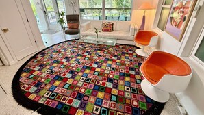 Un salon avec une table basse ronde, deux fauteuils, un canapé et un tapis coloré.