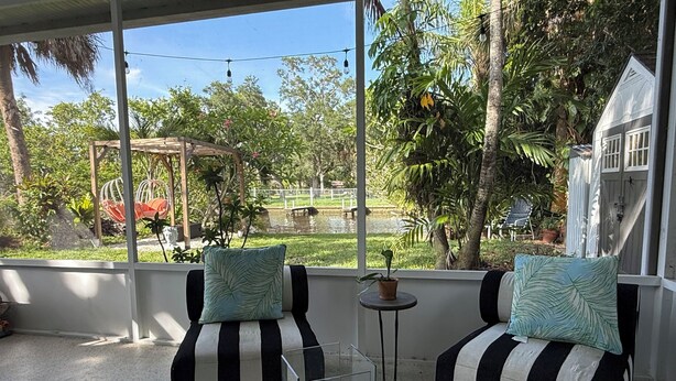 Une pièce avec deux canapés rayés de noir et de blanc, une petite table avec un plateau en verre et une vue sur un jardin avec des arbres et un étang.