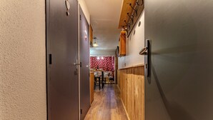 Un pasillo estrecho con piso de madera, un comedor con pared de estampado rojo y un refrigerador a la derecha.