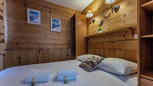 Habitación con paneles de madera, una cama, dos toallas, un cojín, una lámpara de pared y dos cuadros enmarcados.