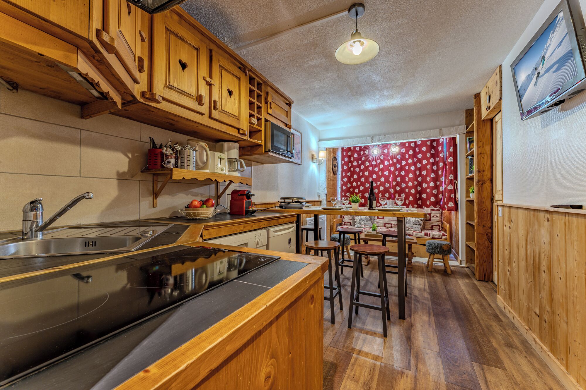A kitchen with wooden cabinets, a stove, a sink, and a dining area with stools.