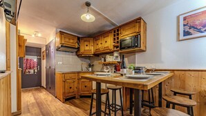 Una cocina pequeña con gabinetes de madera, un microondas y taburetes de bar.