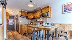 Una cocina compacta con armarios de madera, microondas y una zona de comedor con taburetes.