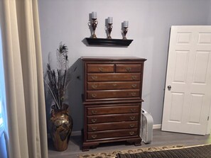 Uma cómoda de madeira com várias gavetas, um vaso decorativo com penas e uma porta branca ao fundo.