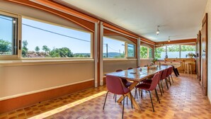 A long dining table with chairs, large windows, and a brick floor.