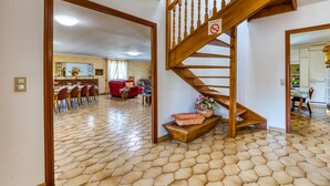A spacious living area with a wooden staircase, a dining area, and a kitchen in the background.