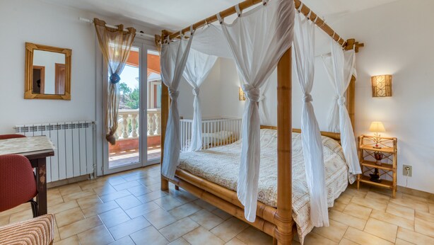 A four-poster bed with a canopy, a wooden nightstand with a lamp, a red chair, and a table with a mirror.
