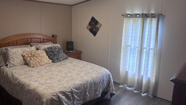 Un dormitorio con cama, mesita de noche, un reloj de pared y una ventana con cortinas.