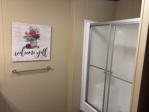 Une salle de bain avec un mur de couleur beige, une porte de douche en verre et un panneau d’accueil orné de motifs floraux.