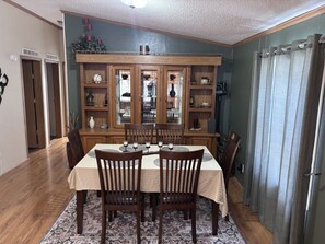 A dining room with a wooden table, chairs, and a glass-fronted cabinet with shelves.