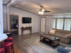 A living room with a television, a couch, a coffee table, and a dining area with stools. - Reindeer Crossing - Prancer Blue - 1.5 mi to HW (Dale)