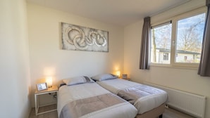 Ett sovrum med två sängar, en stor abstrakt målning på väggen, sänglampor och ett fönster med gardiner.