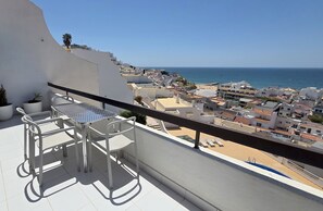 A balcony with a table and chairs, overlooking a coastal town and the sea. - Sunset View Albufeira 53 (Albufeira)