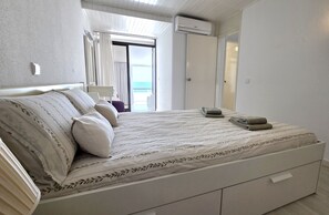Ein Schlafzimmer mit Bett, Nachttisch, Fenster mit Vorhängen und einer Tür, die auf einen Balkon führt.