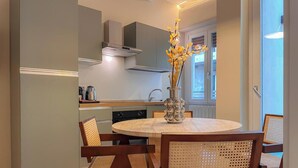 Uma cozinha moderna com área de refeições, incluindo uma mesa redonda e cadeiras, um vaso com flores e uma janela que oferece luz natural.