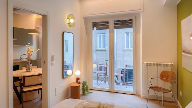 Quarto moderno com cama, mesa de cabeceira com abajur, espelho e vista para a varanda.