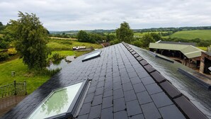 En takterrass med ett takfönster, utsikt över ett lantligt landskap och en byggnad med ett grönt tak.