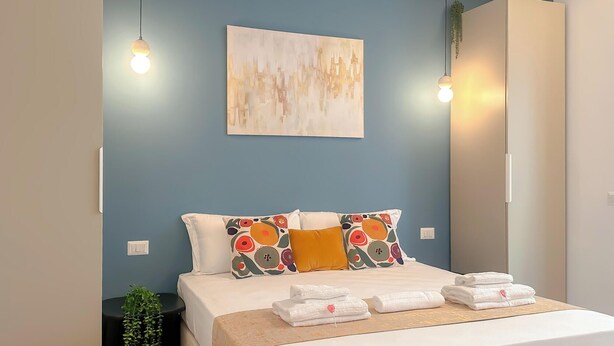 Een slaapkamer met een bed, kussens, een kunstwerk aan de muur en hanglampen.