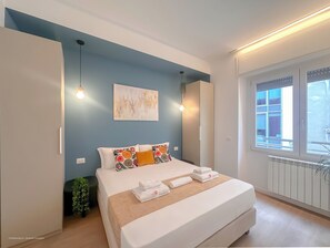 A bedroom with a bed, bedside lamps, a window, and a radiator. - Flatsharing Design Suite - Indaco (Milan)
