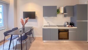 Een moderne keuken met grijze kastjes, een inbouwoven, een spoelbak en een flatscreen televisie aan de muur.