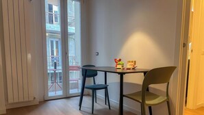 Een eethoek met een tafel en stoelen, een schuifdeur naar een balkon en een kleine tafel met een vaas en fruit.