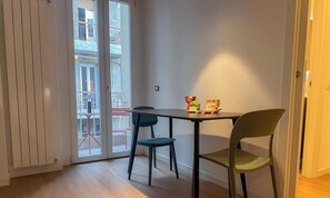 A dining area with a table and chairs, a sliding glass door leading to a balcony, and a small table with a vase and fruit. - Flatsharing Design Suite - Rubino (Milan)