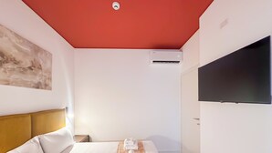 Een hotelkamer met een bed, een wandtelevisie, een airconditioning en een schilderij aan de muur.