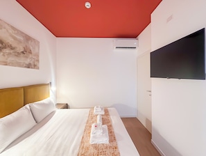 A hotel room with a bed, a flat-screen TV mounted on the wall, an air conditioning unit, and a painting on the wall. - Flatsharing Design Suite - Rubino (Milan)