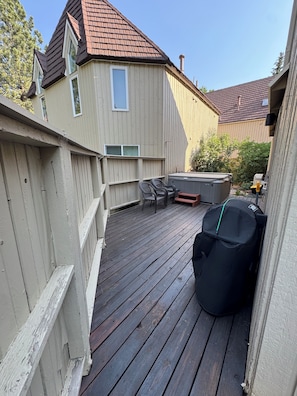 Eine Holzterrasse mit Gartenmöbeln, einem Whirlpool und einem überdachten Grillbereich.