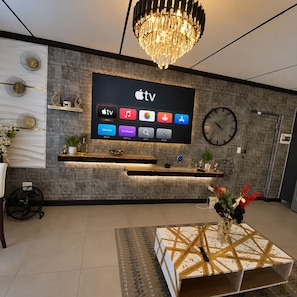 Moderni olohuone, jossa on seinälle asennettu taulutelevisio, kattokruunu ja seinäkello.