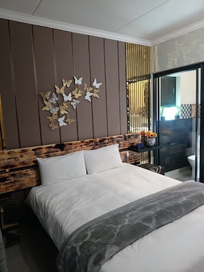 Een moderne slaapkamer met een bed, een hoofdbord met houtmotief, een vlinderdecoratie aan de muur en uitzicht buiten door een glazen deur.