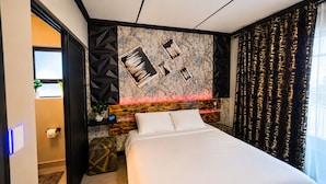 Una habitación de hotel moderna con una cama grande, un cabecero con diseños geométricos, una pared con arte abstracto y una ventana con cortinas.