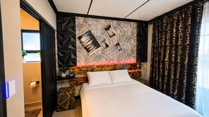 Moderni hotellihuone, jossa on suuri sänky, geometrisin kuvioin koristeltu pääty, abstraktitaiteella koristeltu seinä ja ikkuna, jossa on verhot.
