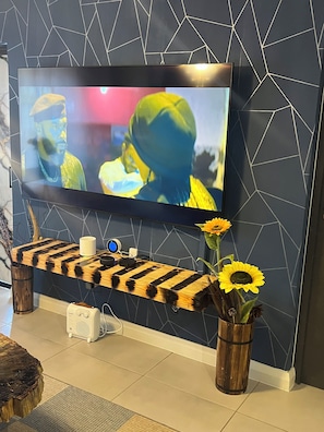 Een televisie bevestigd aan een muur met een geometrisch patroon, een houten plank met een streependesign, en twee vazen met zonnebloemen.