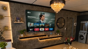 Una sala de estar moderna con un televisor de pantalla plana mostrando un programa, una araña, un reloj redondo y una lavadora integrada.