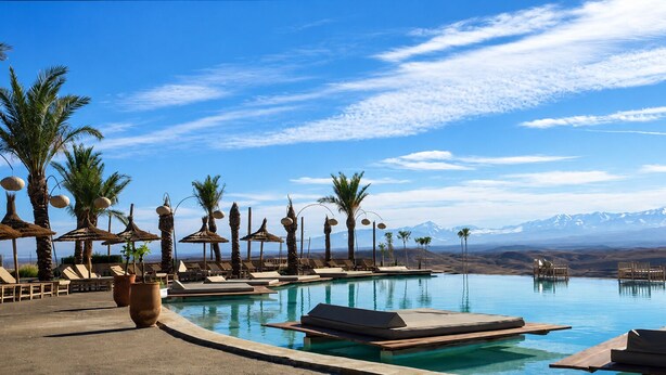 A poolside area with lounge chairs, palm trees, and a mountain view. - Sunset Agafay (Agafay)