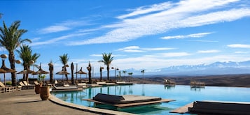 A poolside area with lounge chairs, palm trees, and a mountain view.